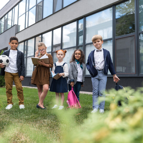 group of beautiful multiethnic children standing near school and looking at camera